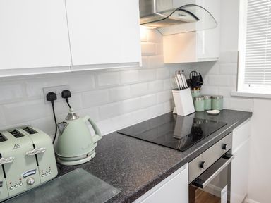 A kitchen countertop with a toaster, kettle, knife block, cooking utensils, and canisters near a stove at Little Retreat in Liskeard