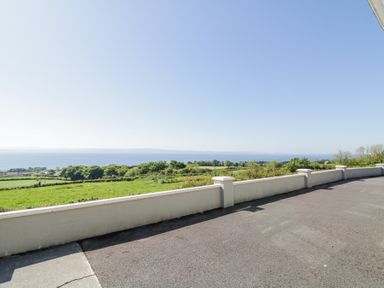 A paved outdoor area with a low wall overlooking green fields and a large body of water at Tullyally in Redcastle