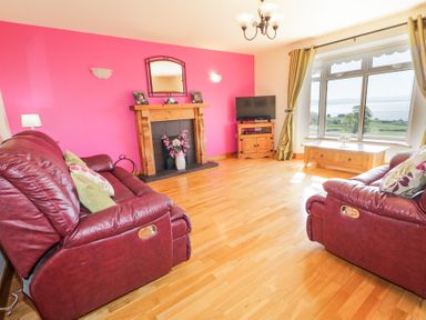 A living room with two red leather sofas wooden fireplace and a large window with curtains at Tullyally in Redcastle