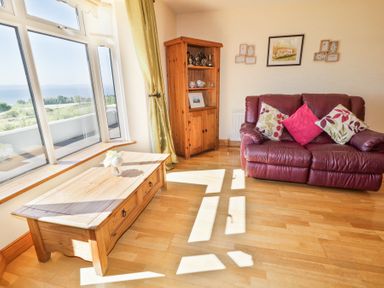 A living room with a large window a wooden coffee table a wooden cabinet and a red leather sofa with cushions at Tullyally in Redcastle