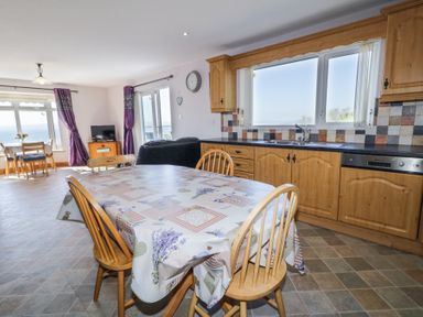 A kitchen and dining area with a wooden table and chairs a large window cabinets and a TV in the background at Tullyally in Redcastle