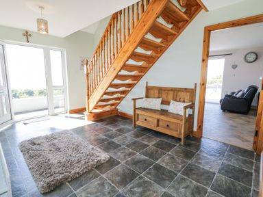 A hallway with tiled floor wooden staircase and wooden bench with cushions at Tullyally in Redcastle