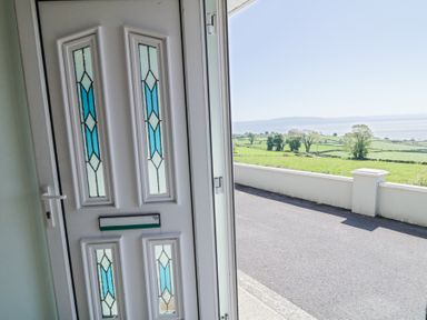 A white front door with blue stained glass panels opening to a road and green fields with trees and water in the distance at Tullyally in Redcastle