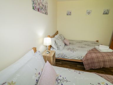 A bedroom with two beds with floral bedding a wooden nightstand with a lamp and folded towels on one bed at Tullyally in Redcastle