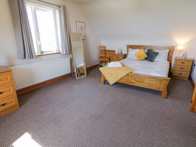 A bedroom with a wooden bed and nightstands a floor mirror and a window with curtains at Tullyally in Redcastle