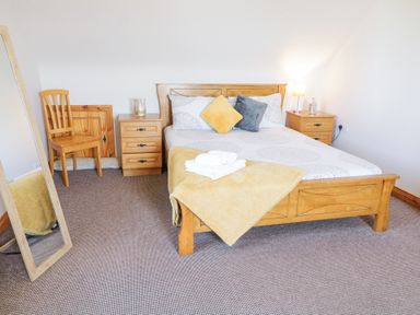 A bedroom with a wooden bed with pillows and a blanket two bedside tables with lamps a chair and a full-length mirror at Tullyally in Redcastle