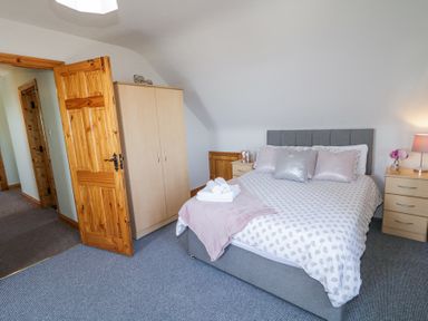 A bedroom with a double bed two bedside tables a wardrobe and an open wooden door at Tullyally in Redcastle