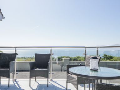 Outdoor balcony with glass railing wicker chairs and a round glass table with a lantern at Tullyally in Redcastle