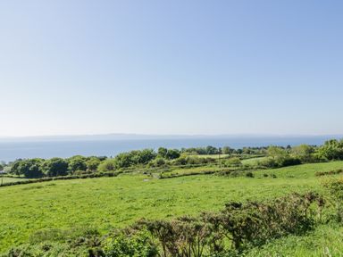 A hillside view of green fields and trees with a body of water and distant land at Tullyally in Redcastle