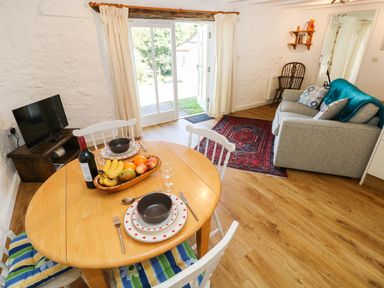 A dining area with a wooden table set for two and a living space with a sofa and a red rug near glass doors at The Granary Cottage in Llangrannog near Cardigan
