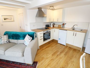 A kitchen area with white cabinets and wooden countertop next to a grey sofa with cushions at The Granary Cottage in Llangrannog near Cardigan