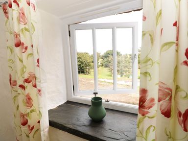 A window with floral curtains and a green vase on the windowsill at The Granary Cottage in Llangrannog near Cardigan