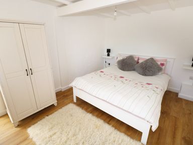 A bedroom with a double bed with floral duvet and gray pillows a white wardrobe and a fluffy rug on wooden floor at The Granary Cottage in Llangrannog near Cardigan