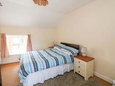 A bedroom with a double bed with striped bedding and two bedside tables with lamps at Grange Farmhouse in Fethard-on-Sea County Wexford