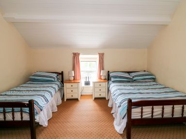 A bedroom with two beds a window in the middle and two bedside cabinets with lamps at Grange Farmhouse in Fethard-on-Sea County Wexford