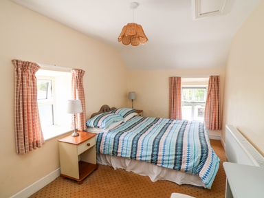 A bedroom with a double bed bedside tables lamps windows with curtains and a radiator at Grange Farmhouse in Fethard-on-Sea County Wexford