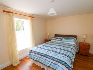 A bedroom with a double bed with patterned bedding two bedside tables with lamps and a window with curtains at Grange Farmhouse in Fethard-on-Sea County Wexford