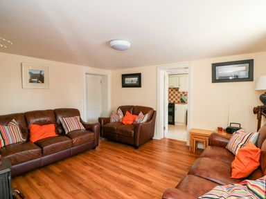 A living room with three brown leather sofas with colorful pillows and wooden flooring at Grange Farmhouse in Fethard-on-Sea County Wexford