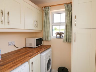 A utility room with a washing machine microwave cabinets a window with green check curtains and a horse sculpture on the sill at Grange Farmhouse in Fethard-on-Sea County Wexford