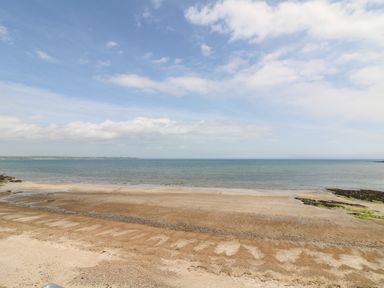 A sandy beach with a calm sea and partly cloudy sky at Grange Farmhouse in Fethard-on-Sea County Wexford