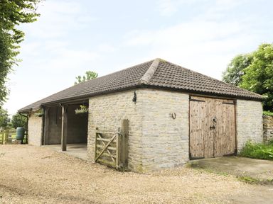 A stone barn with wooden doors and hanging flower baskets at The Old Goat Barn at Trout Cottage in Somerton
