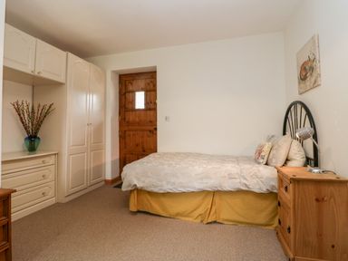 A bedroom with a single bed table lamp wardrobe and wooden door at The Old Goat Barn at Trout Cottage in Somerton
