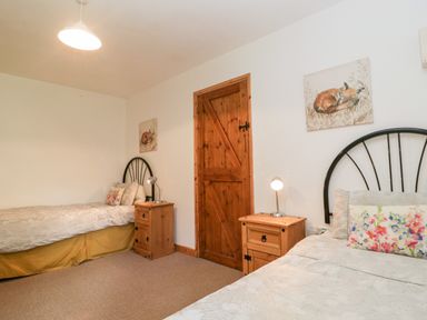 A bedroom with two single beds wooden nightstands a wooden door and paintings of foxes at The Old Goat Barn at Trout Cottage Somerton