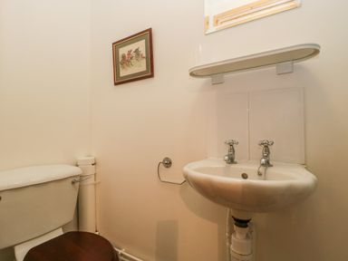 A small bathroom with a toilet and a sink with two taps and a shelf above at The Old Goat Barn at Trout Cottage in Somerton