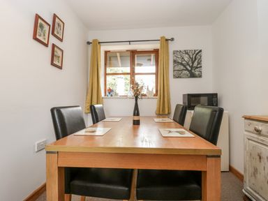 A dining room with a wooden table and four black chairs near a window with yellow curtains at The Old Goat Barn at Trout Cottage in Somerton