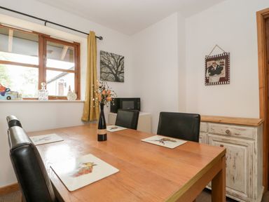 A dining room with a wooden table black chairs placemats a vase with flowers a window and a cabinet at The Old Goat Barn at Trout Cottage Somerton