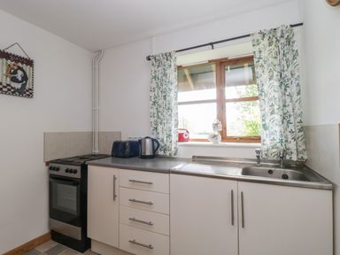 A kitchen with a stove sink countertop toaster kettle and floral curtains at The Old Goat Barn at Trout Cottage Somerton