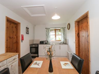 A kitchen with a wooden table and black chairs with a vase on the table and appliances near a window at The Old Goat Barn at Trout Cottage Somerton