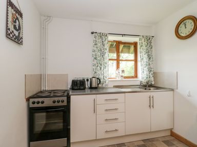 A kitchen with an oven and countertop with toaster kettle and sink under a window with floral curtains at The Old Goat Barn at Trout Cottage in Somerton