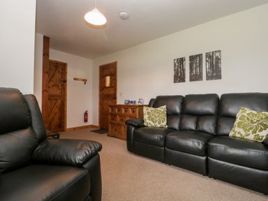 A living room with black leather sofas wooden doors a wooden cabinet and wall art at The Old Goat Barn at Trout Cottage in Somerton