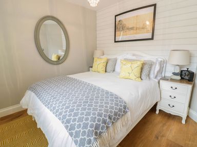 A bedroom with a bed with yellow and gray pillows a blue patterned throw a round mirror and a nightstand with a lamp and clock at Oh Buoy in Charlestown