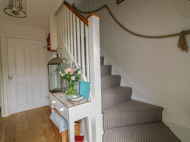 A staircase with striped carpet next to a hallway table holding a lantern a vase with flowers and a basket below at Oh Buoy in Charlestown