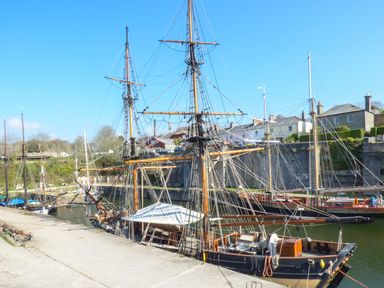A dock with wooden sailing ships and buildings in the background at Oh Buoy in Charlestown