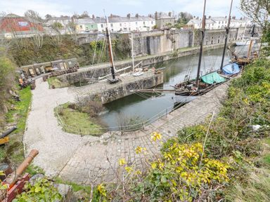 A narrow canal with two docked sailing ships and stone walkway surrounded by houses and greenery at Oh Buoy in Charlestown
