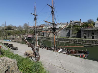 A dock with moored tall ships and barrels near old stone buildings at Oh Buoy in Charlestown