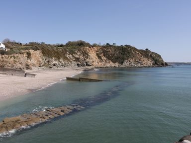 A beach with rocky cliffs and a stone breakwater extending into the sea at Oh Buoy in Charlestown