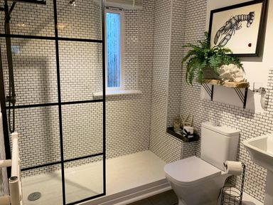 A bathroom with a walk-in shower separated by a glass panel a toilet and a sink with tiled walls and a framed lobster picture at Oh Buoy in Charlestown