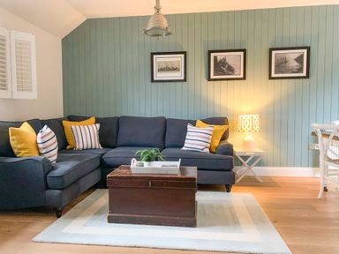 A living room with a dark corner sofa with cushions and a wooden chest coffee table on a rug at Oh Buoy in Charlestown