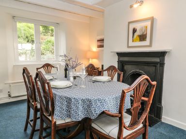 A dining room with a table covered in a patterned tablecloth surrounded by chairs and set with plates and glasses at Clamoak Cottage in Clamoak near Bere Alston