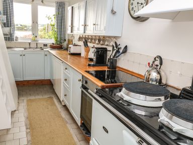 A kitchen with white cabinets wooden countertop a stove a kettle and a plant by the window at Clamoak Cottage Clamoak near Bere Alston