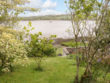 A garden with trees and shrubs overlooking a body of water with a boat and hills in the background at Clamoak Cottage Clamoak near Bere Alston