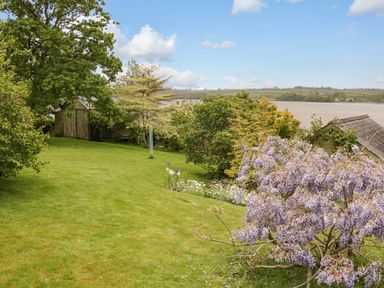 A garden with grass trees flowers and a shed near a body of water at Clamoak Cottage in Clamoak near Bere Alston