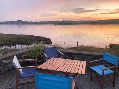 An outdoor seating area with four chairs and a wooden table overlooking a river at sunset at Clamoak Cottage in Clamoak near Bere Alston