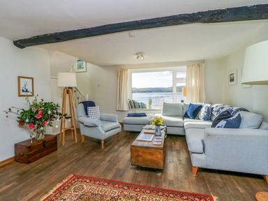 A living room with a sectional sofa armchair wooden coffee table flowers and a view of the water at Clamoak Cottage in Clamoak near Bere Alston