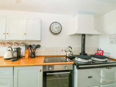 A kitchen with white cabinets wooden countertop a stove oven kettle coffee machine and a wall clock at Clamoak Cottage in Clamoak near Bere Alston