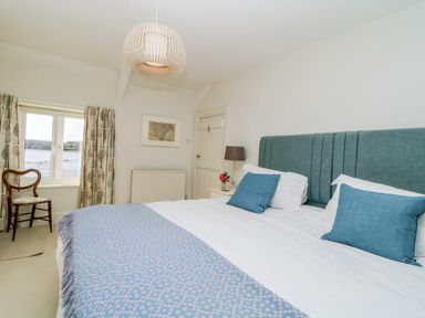 A bedroom with a large bed blue headboard blue pillows and a window with tree patterned curtains at Clamoak Cottage in Clamoak near Bere Alston